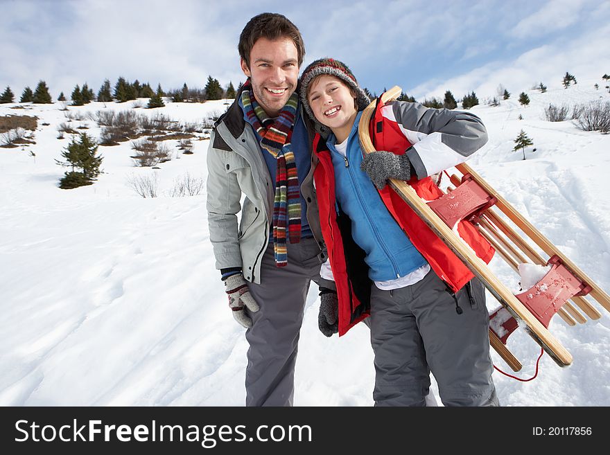 Young Father And Son In Snow With Sled smiling at camera