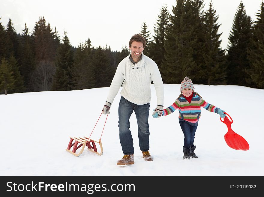 Young Father And Daughter Walking In Snow With Sleds