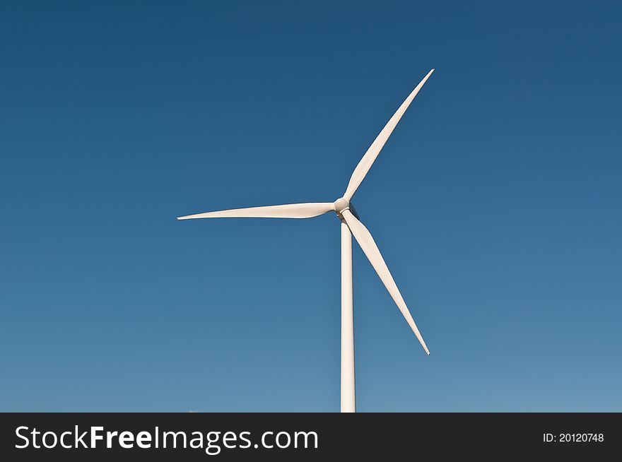 A large wind turbine spins with a deep blue sky in the background. A large wind turbine spins with a deep blue sky in the background.