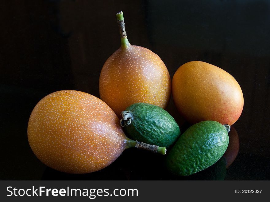 A selection of exotic fruit including granadillas, feijoas & plum mango, against a black granite background