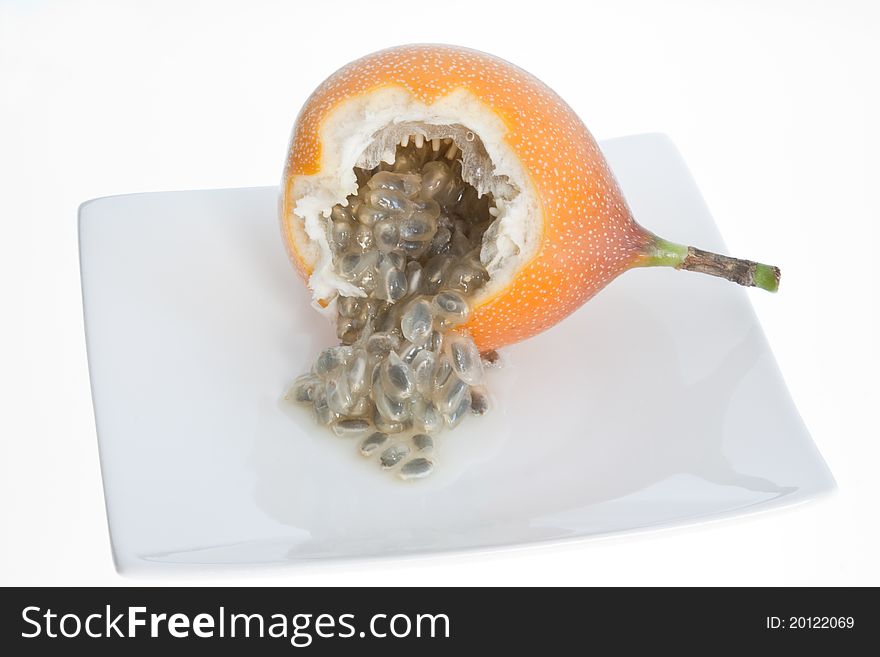 An opened granadilla showing the seeds inside on a white plate. An opened granadilla showing the seeds inside on a white plate