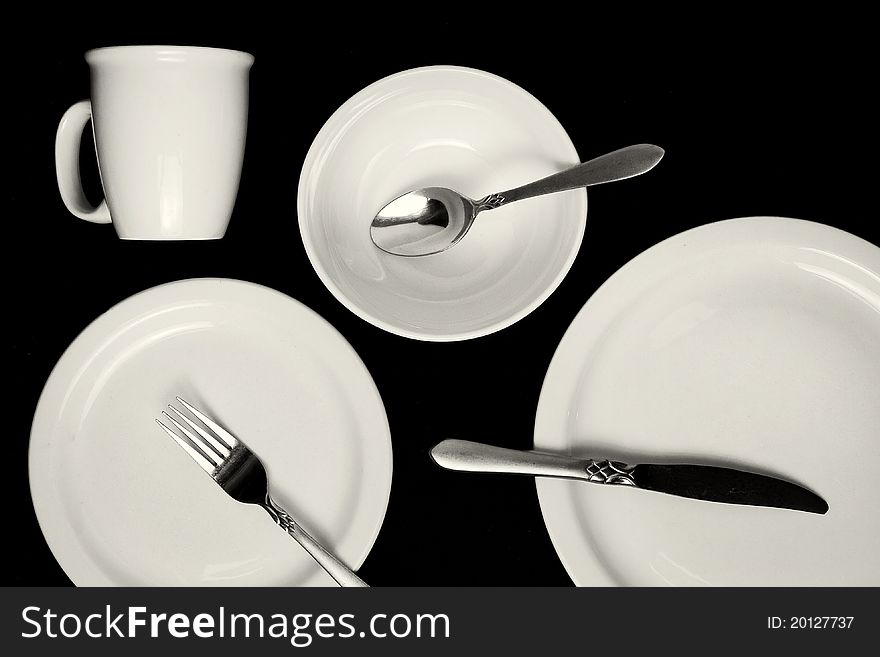 A set of clean white dishers and silverware on a black table. A set of clean white dishers and silverware on a black table.