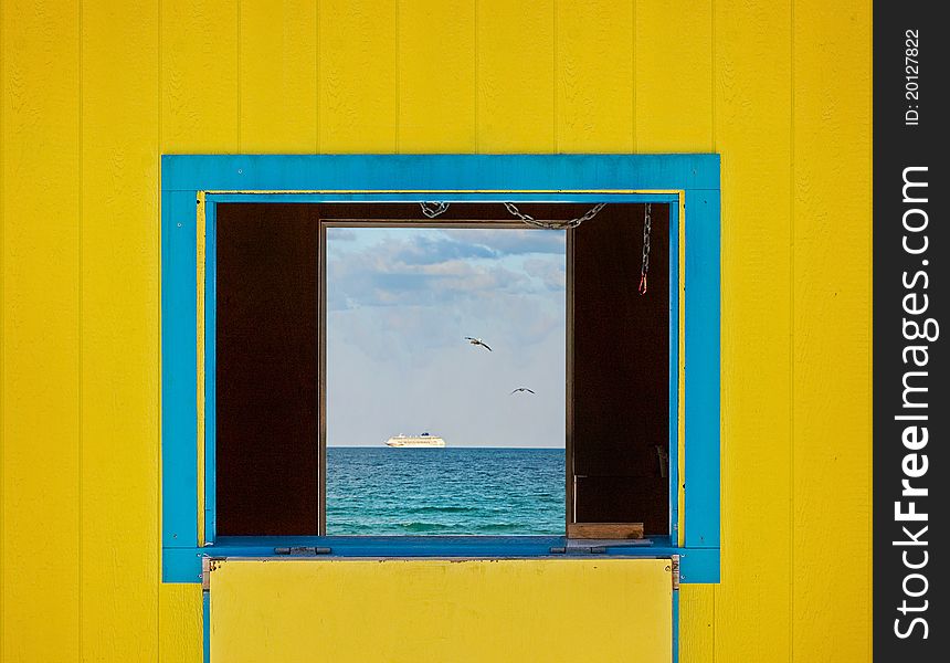 Colorful summer image of the ocean waters and blue sky framed by yellow lifeguard house window. Architectural details