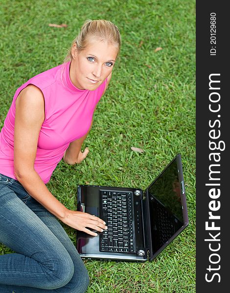 Young attractive woman works on her laptop at the park and looks up