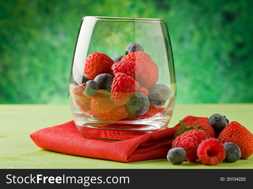 Photo of delicious berries inside a crystal glass in front of green background