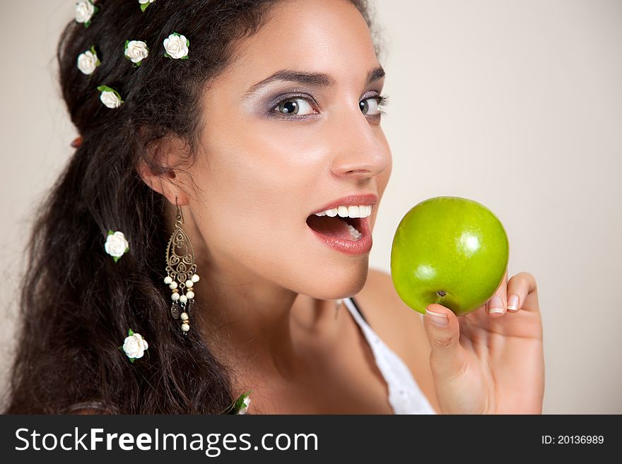 Beautiful Mixed race Woman with small white flowers in her hair eating an apple isolated on beige. Beautiful Mixed race Woman with small white flowers in her hair eating an apple isolated on beige