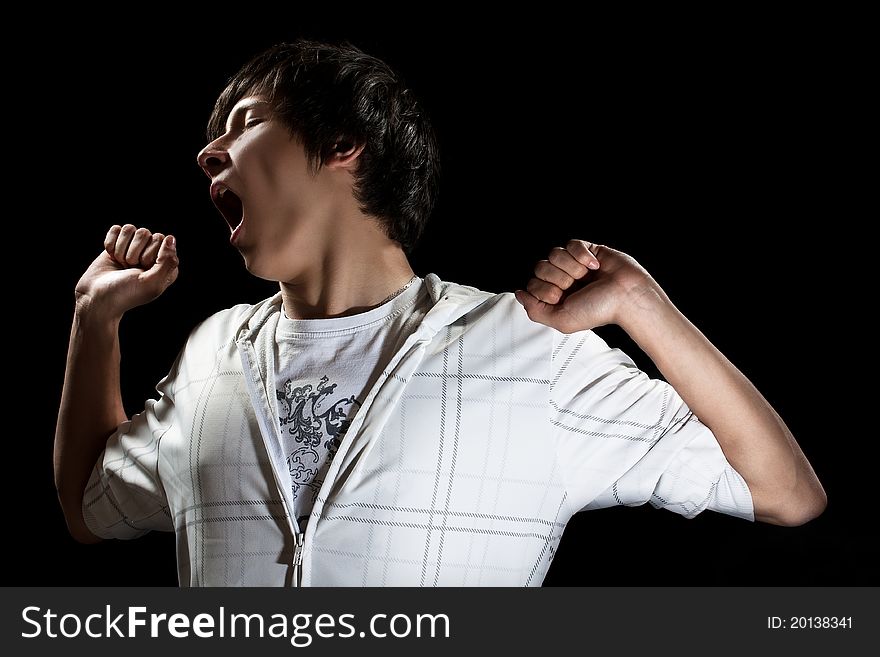 Standing young man yawning and stretching , isolated on black. Standing young man yawning and stretching , isolated on black