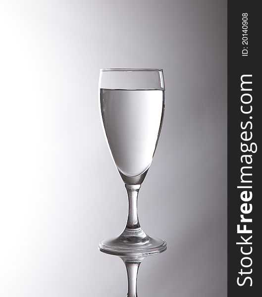 A simple fresh glass of water mirrored over a white to grey blended Background. A simple fresh glass of water mirrored over a white to grey blended Background