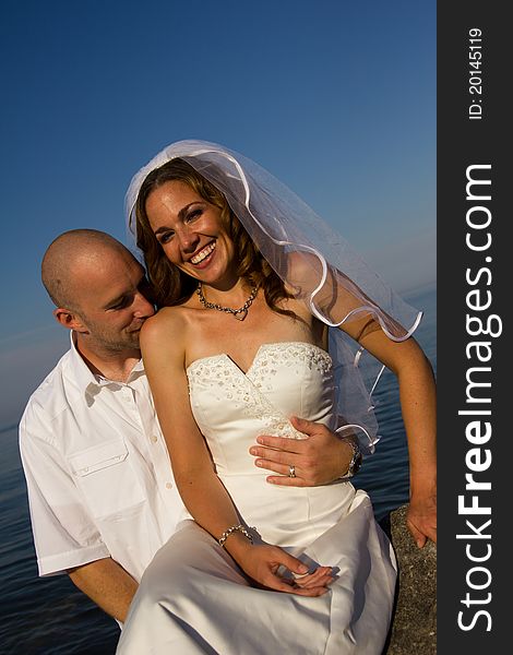 A groom kissing brides shoulder on rock at beach. A groom kissing brides shoulder on rock at beach