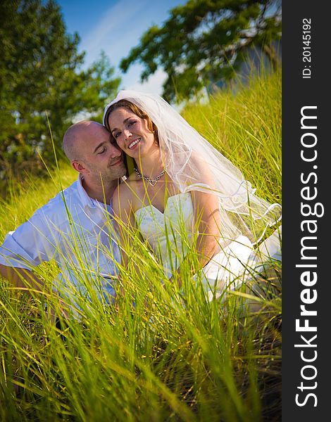 A groom and bride sitting in long grass. A groom and bride sitting in long grass