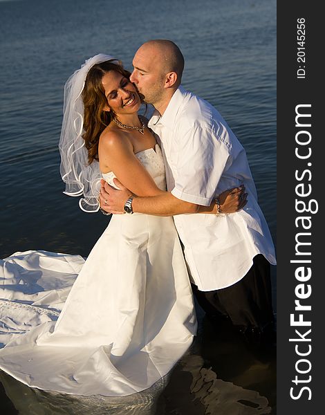 A groom kissing brides cheek while standing in water. A groom kissing brides cheek while standing in water