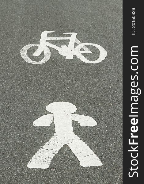 White painted symbols depicting a person and a bicycle on a grey surface of a tarmac track. White painted symbols depicting a person and a bicycle on a grey surface of a tarmac track.