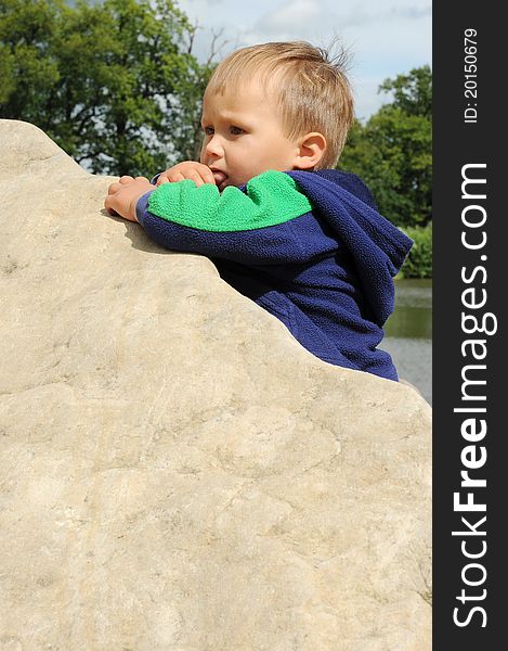 Little boy climbing a big stone, having thumb in mouth. Little boy climbing a big stone, having thumb in mouth