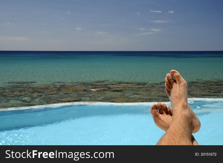 Picture of male legs over swimming pool and sea in the background