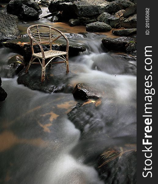 Long exposure rattan chair at waterfall create slow motion water flow. Chair face to right side. position chair at top left at image.