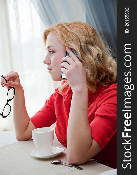 Young blond girl in cafe is drinking coffee and is speaking by mobile phone. Young blond girl in cafe is drinking coffee and is speaking by mobile phone