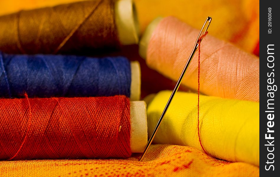 Needle on the yellow-red cloth with yarn in the back of it. Needle on the yellow-red cloth with yarn in the back of it