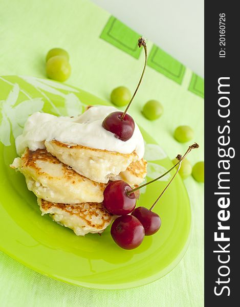 Pancakes with cherries and cream on green plate