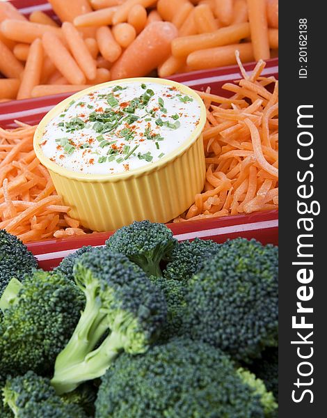 Variety of raw carrots and broccoli in a red ceramic dish with ranch dip and garnish