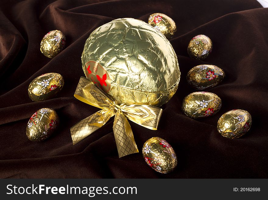 Close up view of sweet golden eggs of chocolate spread on a dark brown silk background. Close up view of sweet golden eggs of chocolate spread on a dark brown silk background.