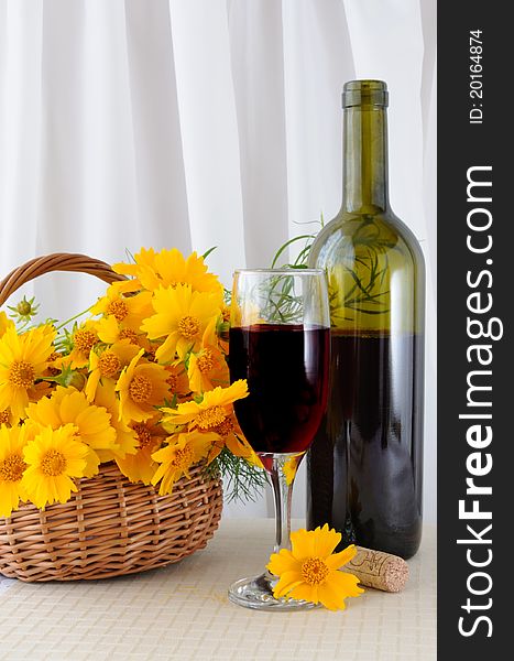 A glass of rose wine with an open bottle and yellow flowers in a basket. A glass of rose wine with an open bottle and yellow flowers in a basket