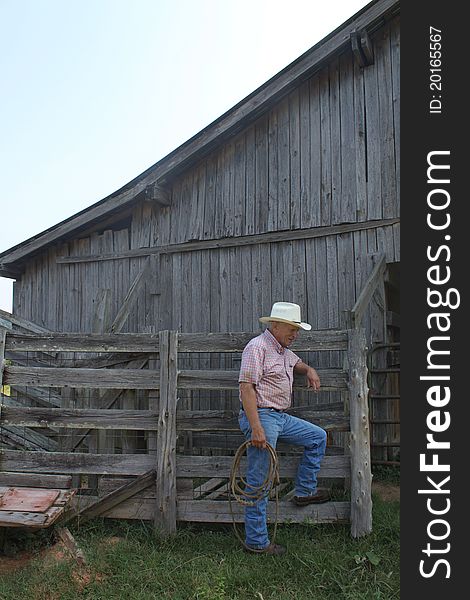 Large animal vet looks like a cowboy as he leans against a fence by the barn holding his lasso.