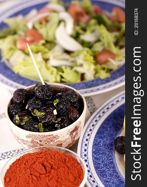 Close up view of a some tempered dry black olives and a salad.