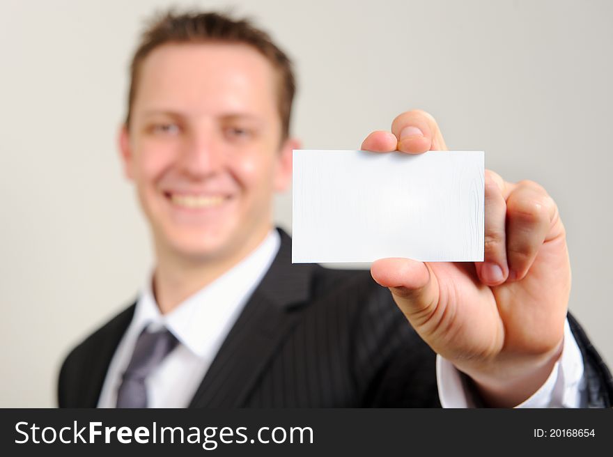 Ambitious white man in business suit smiles confidently and holds out his business card; selective focus on card. Ambitious white man in business suit smiles confidently and holds out his business card; selective focus on card