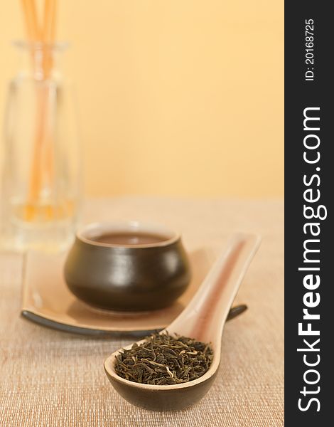 Black tea leaves on spoon, tea in tea bowl in background. Black tea leaves on spoon, tea in tea bowl in background.