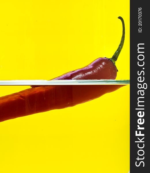 Long red chili floating in the glass with yellow background