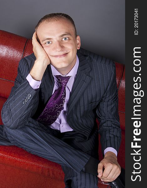 Thoughtful young man in a suit sitting on a red couch. Thoughtful young man in a suit sitting on a red couch