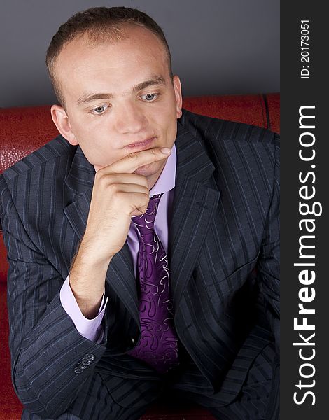 Thoughtful guy in a suit sitting on a red couch