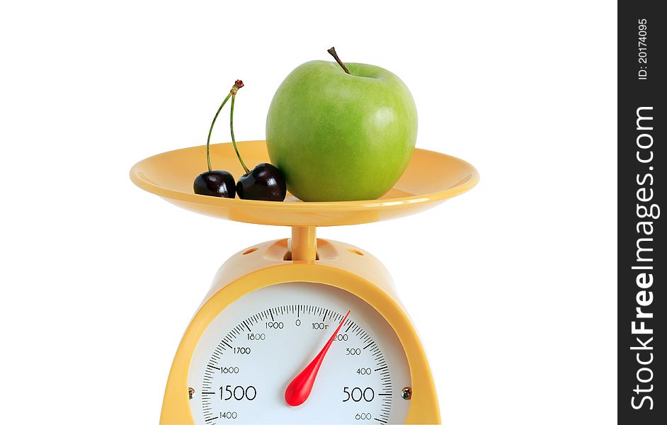 Green apple and cherry lying on yellow kitchen scale. Isolated on white background with clipping path. Green apple and cherry lying on yellow kitchen scale. Isolated on white background with clipping path