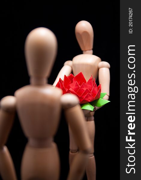 A wooden mannequin giving hand-made paper flower to another mannequin. Shallow DOF, focus is on the flower. This photo made over black background but is not isolated. A wooden mannequin giving hand-made paper flower to another mannequin. Shallow DOF, focus is on the flower. This photo made over black background but is not isolated.