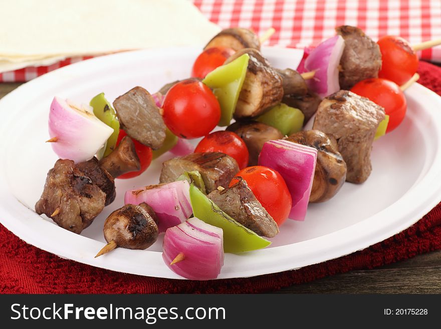 Beef kabobs with onion, peppers, tomatoes,and mushrooms on a plate