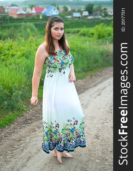 The portrait of young smiling girl in light dress on the road