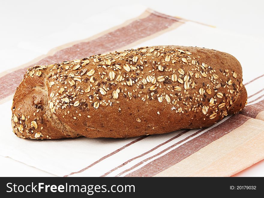 Long loaf of rye bread strewed by sunflower seeds on a white background