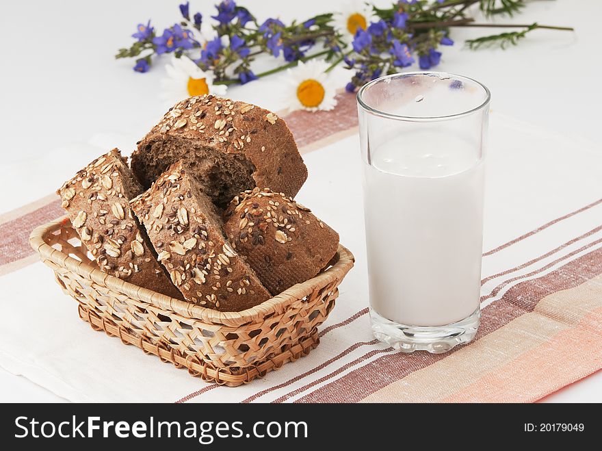 Summer Breakfast. The cut black bread in a basket, a glass of milk and a small summer bouquet on a linen towel. Summer Breakfast. The cut black bread in a basket, a glass of milk and a small summer bouquet on a linen towel