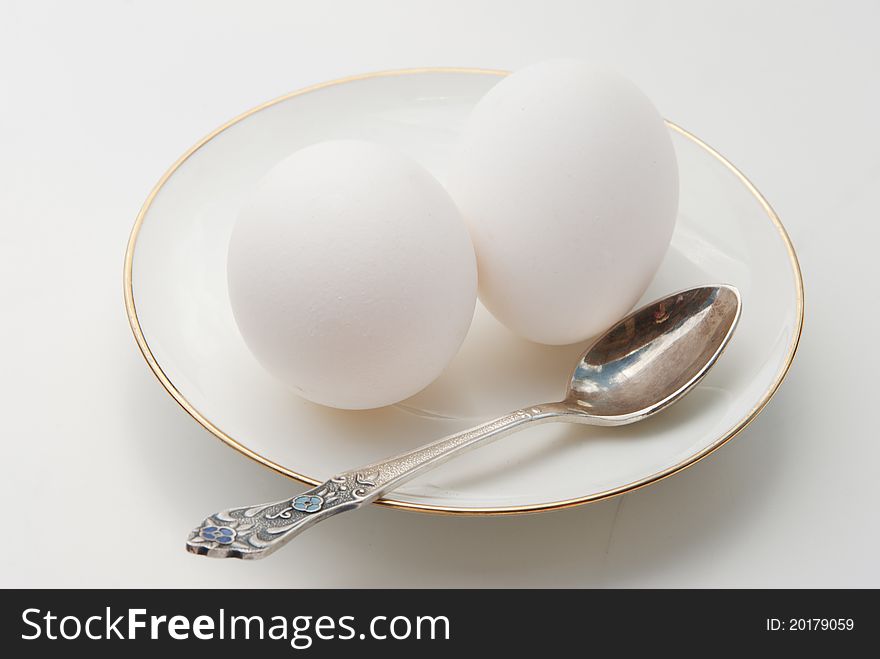 Breakfast. Two white eggs on a white plateau and a spoon on a light background. Breakfast. Two white eggs on a white plateau and a spoon on a light background