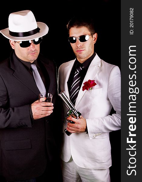 View of two gangster males holding a gun on a black background. View of two gangster males holding a gun on a black background.