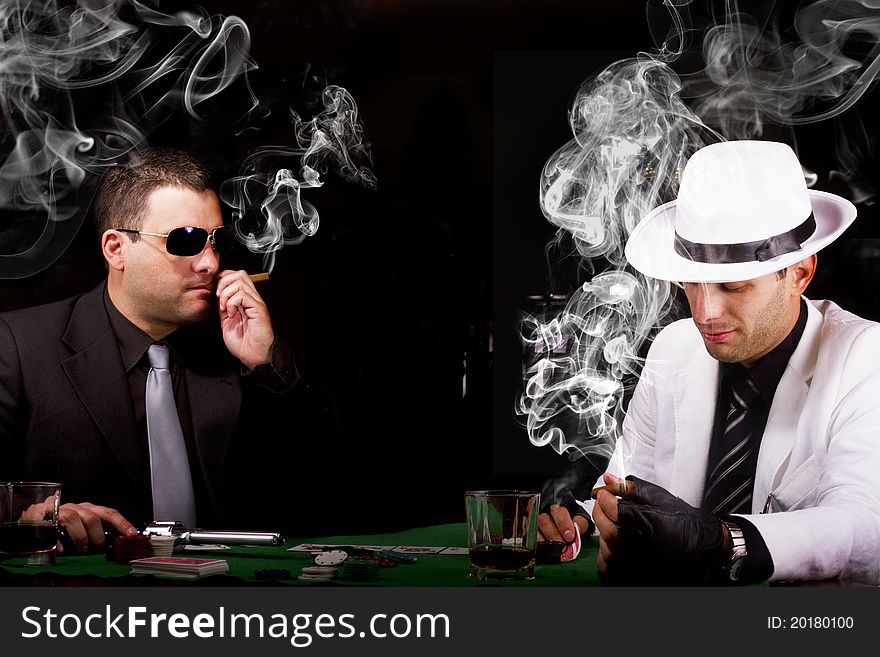 View of two gangster males playing some poker and smoking Cuban cigars. View of two gangster males playing some poker and smoking Cuban cigars.