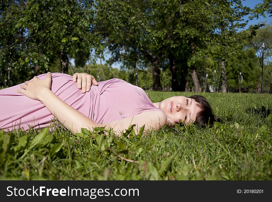 The young pregnant girl in park, has a rest on a grass. The young pregnant girl in park, has a rest on a grass