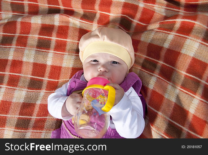 The portrait of the kid, lays on on a coverlet and drink water