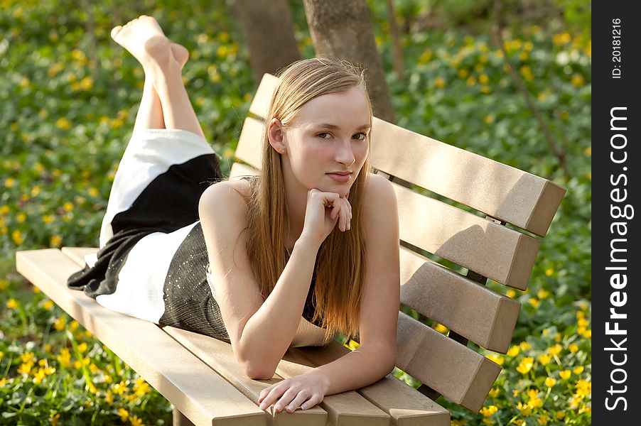 A portrait of a beautiful teenage girl lying on a park bench in a gorgeous dress, surrounded by flowers. A portrait of a beautiful teenage girl lying on a park bench in a gorgeous dress, surrounded by flowers