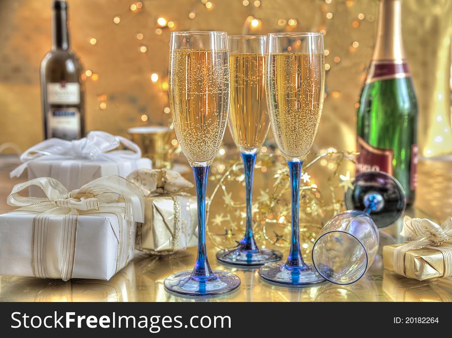 Champagne in glasses,gift boxes,bottles of wine on gold background with twinkle lights. Champagne in glasses,gift boxes,bottles of wine on gold background with twinkle lights.