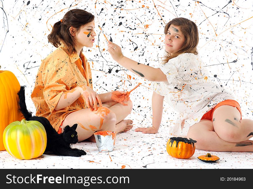 Two sisters deep in black and orange paint, surrounded by pumpkins, a black can and a paint-spattered background. Two sisters deep in black and orange paint, surrounded by pumpkins, a black can and a paint-spattered background.