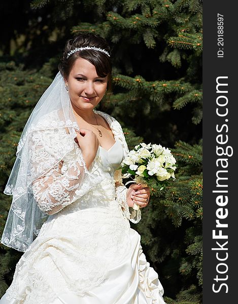 Happy bride on background of green spruce in summer