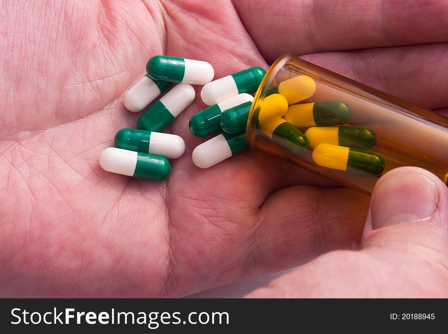 Pill Containers with Green and White capsules inside, poured on a male hand. Pill Containers with Green and White capsules inside, poured on a male hand