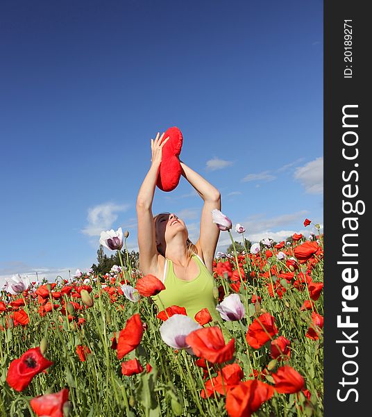 Beautiful blond girl with heart in hands sitting in blooming poppy field. Beautiful blond girl with heart in hands sitting in blooming poppy field