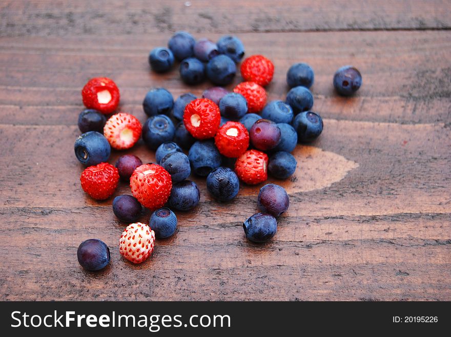 Bilberries and wild strawberries close-up on the wooden background. Bilberries and wild strawberries close-up on the wooden background